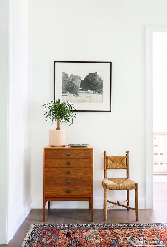 vintage rattan chair, dark brown entry way dresser with black and white artwork on wall. 